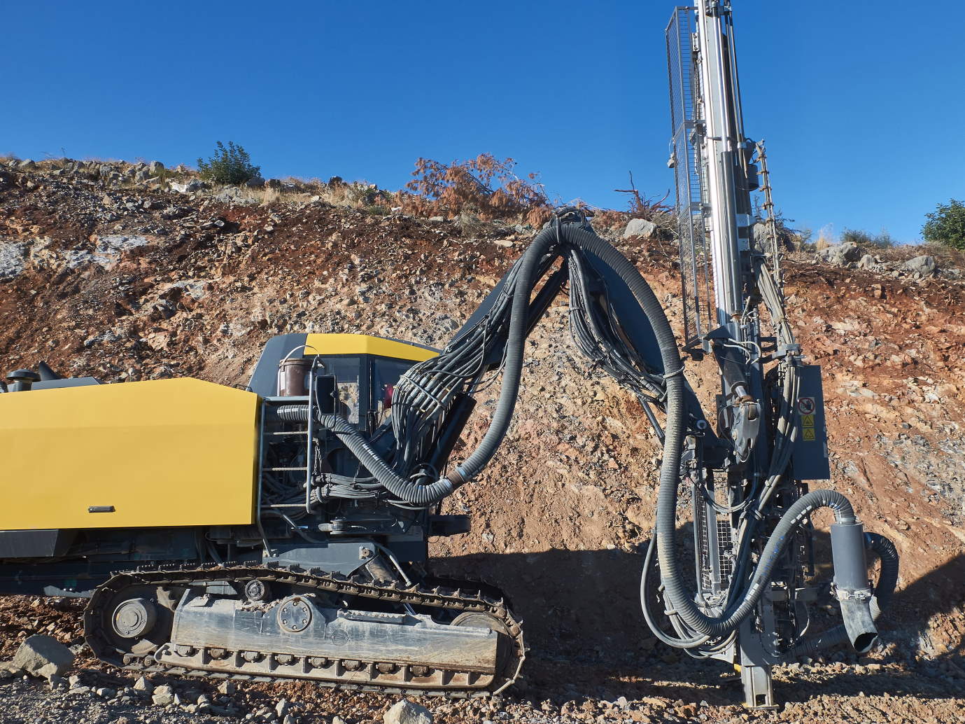 Yellow drilling rig is drilling holes during blasthole drilling operations.
