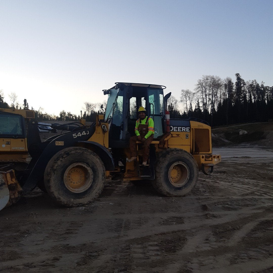 Construction worker sitting and smiling in a wheel loader at a site.